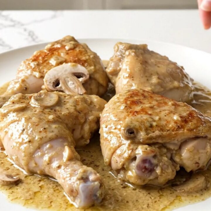 A top-down view of chicken thighs, mushrooms, and creamy sauce in a slow cooker.
