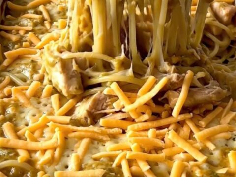 A top-down view of an unbaked spaghetti dish with chicken and creamy sauce, topped with shredded cheddar cheese.