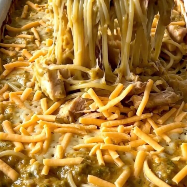 A top-down view of an unbaked spaghetti dish with chicken and creamy sauce, topped with shredded cheddar cheese.