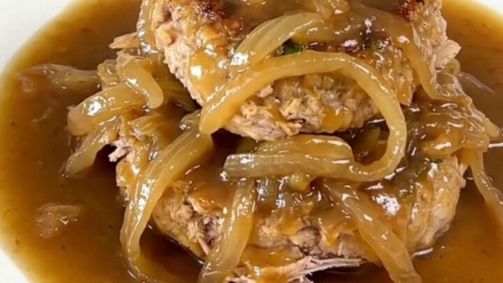 A close-up of slow cooker French onion turkey burger steaks with onions and gravy on a white plate.