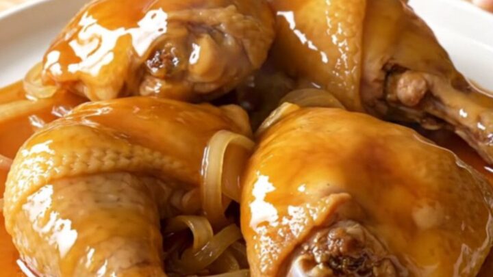 A close-up of tender, braised chicken thighs coated in a glossy, golden hot honey sauce inside a slow cooker.
