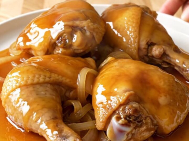 A close-up of tender, braised chicken thighs coated in a glossy, golden hot honey sauce inside a slow cooker.