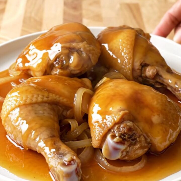 A close-up of tender, braised chicken thighs coated in a glossy, golden hot honey sauce inside a slow cooker.