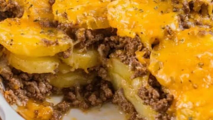 A steaming portion of ground beef and potato casserole being lifted from a white oval dish with stretchy melted cheese.