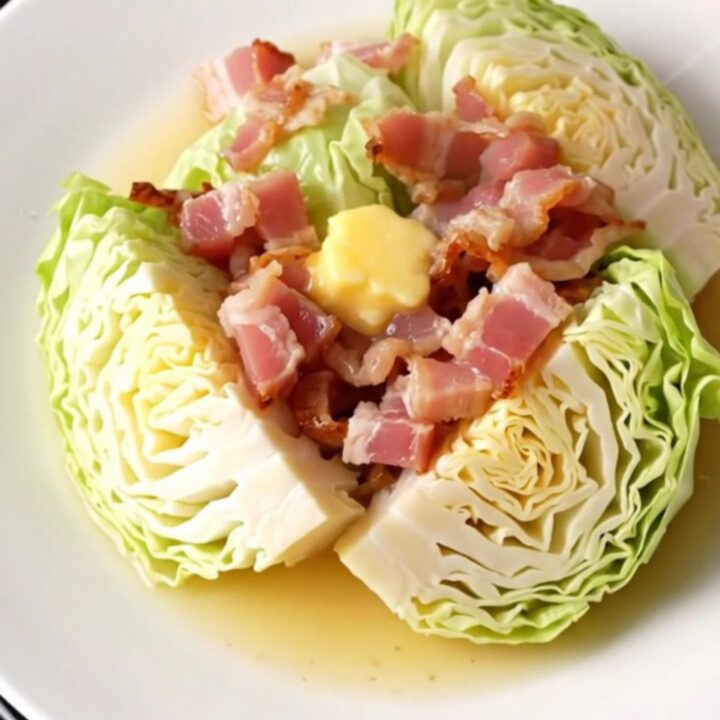A close-up of tender, buttery green cabbage wedges topped with soft, savory bacon pieces in a slow cooker.