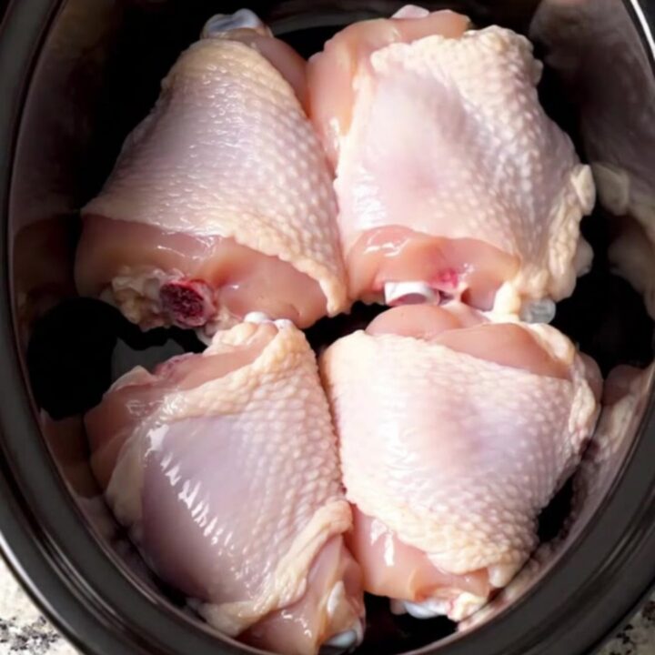 A rustic slow cooker filled with braised chicken thighs, baby potatoes, and green beans in a honey Dijon sauce.