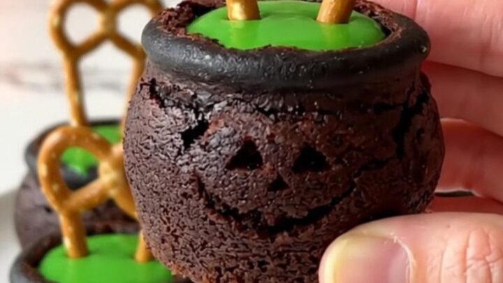 A dozen brownie bite cauldrons filled with green candy and pretzel handles on a white plate.