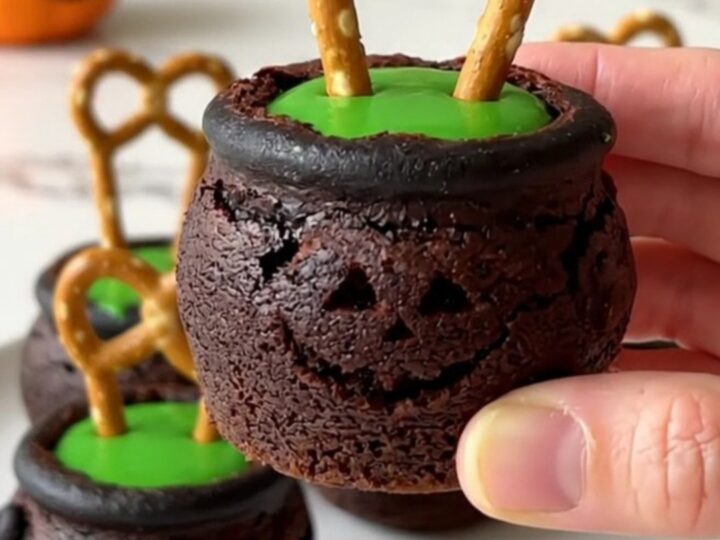A dozen brownie bite cauldrons filled with green candy and pretzel handles on a white plate.