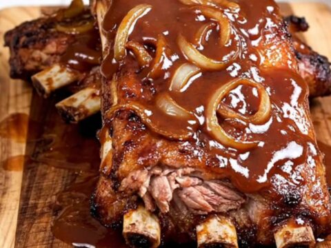A close-up of tender, saucy BBQ spareribs served on a rustic wooden board, showing the meat pulling away from the bone.