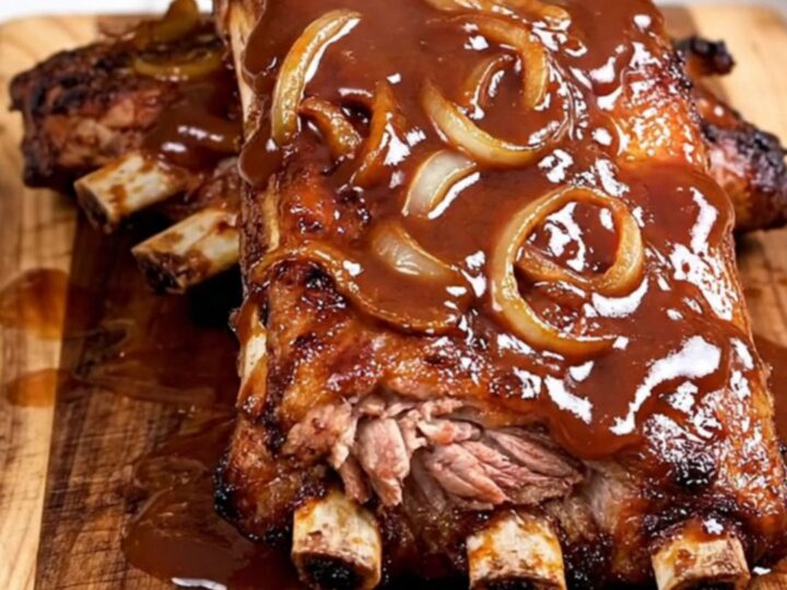 A close-up of tender, saucy BBQ spareribs served on a rustic wooden board, showing the meat pulling away from the bone.