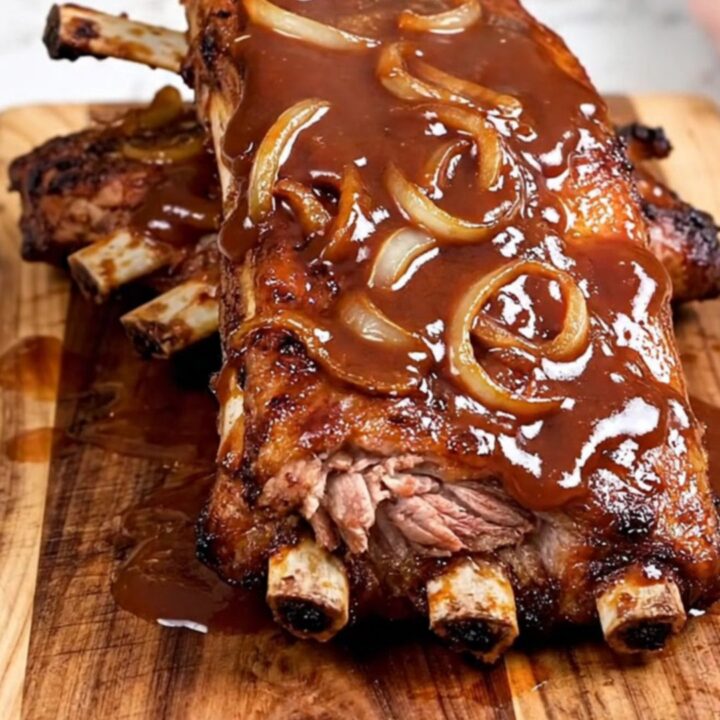 A close-up of tender, saucy BBQ spareribs served on a rustic wooden board, showing the meat pulling away from the bone.