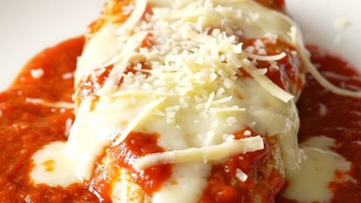 A slow cooker filled with chicken breasts covered in marinara sauce and melted mozzarella and parmesan cheese.
