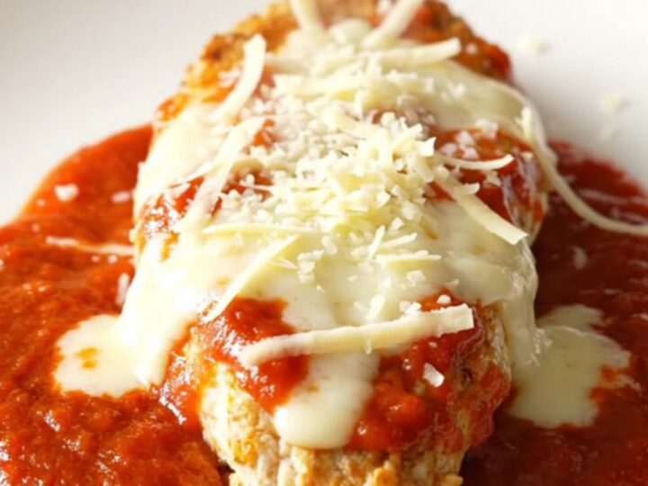 A slow cooker filled with chicken breasts covered in marinara sauce and melted mozzarella and parmesan cheese.