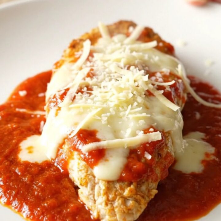 A slow cooker filled with chicken breasts covered in marinara sauce and melted mozzarella and parmesan cheese.