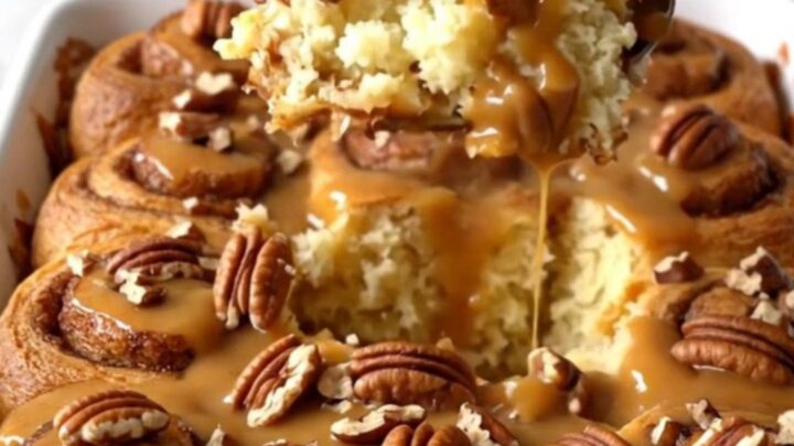 A top-down view of a rectangular ceramic dish filled with unbaked cinnamon roll quarters, brown butter sauce, and pecans.