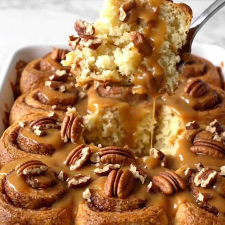 A top-down view of a rectangular ceramic dish filled with unbaked cinnamon roll quarters, brown butter sauce, and pecans.