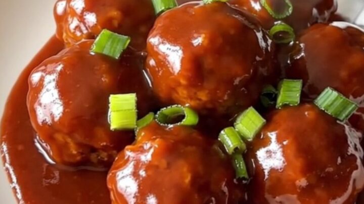 A stainless steel slow cooker filled with turkey meatballs coated in a glossy, vibrant red gochujang honey sauce.