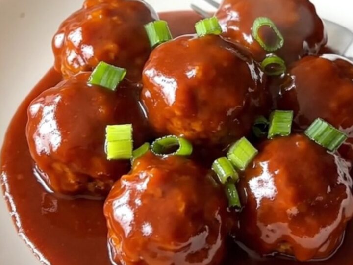 A stainless steel slow cooker filled with turkey meatballs coated in a glossy, vibrant red gochujang honey sauce.