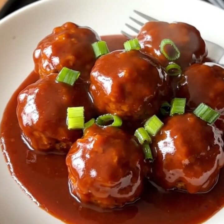 A stainless steel slow cooker filled with turkey meatballs coated in a glossy, vibrant red gochujang honey sauce.