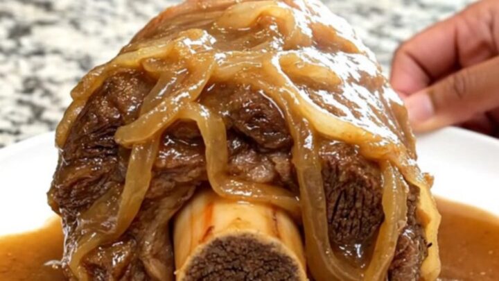 A close-up of a tender bone-in beef shank smothered in rich, brown onion gravy on a white plate.