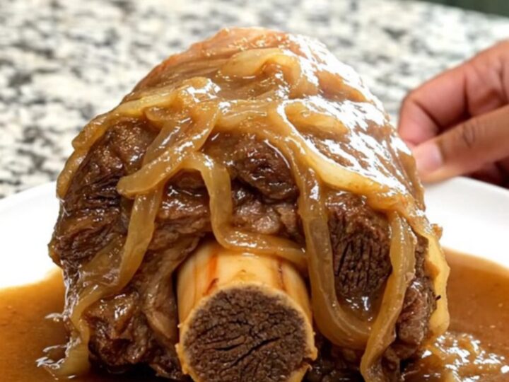 A close-up of a tender bone-in beef shank smothered in rich, brown onion gravy on a white plate.