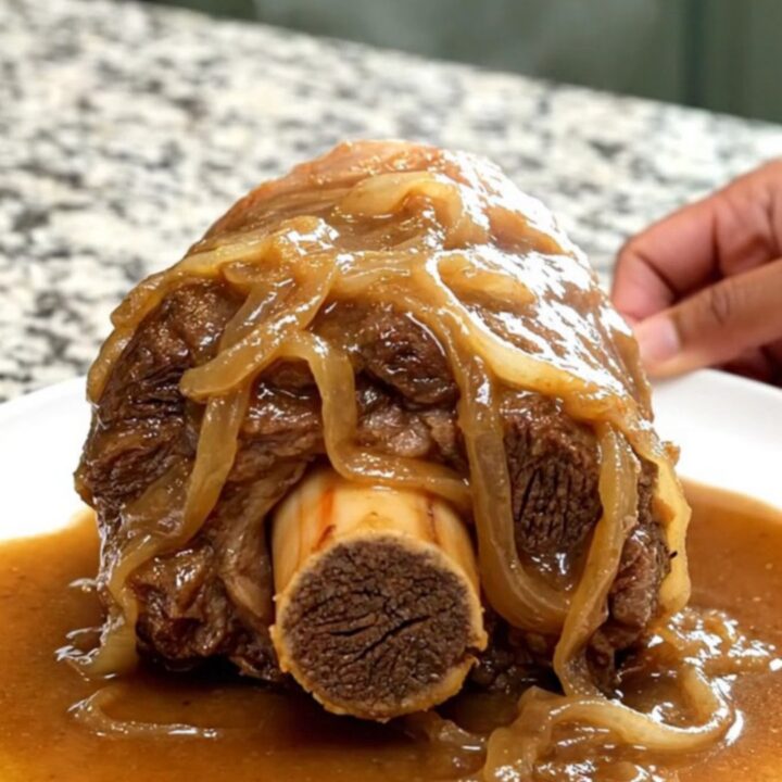 A close-up of a tender bone-in beef shank smothered in rich, brown onion gravy on a white plate.