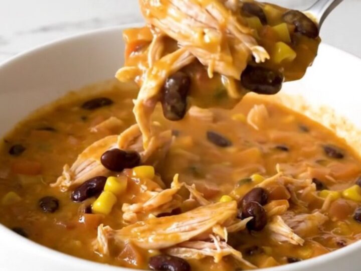 A close-up of creamy chicken chili in a white bowl with a spoon lifting a bite.