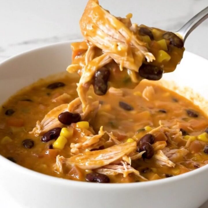 A close-up of creamy chicken chili in a white bowl with a spoon lifting a bite.