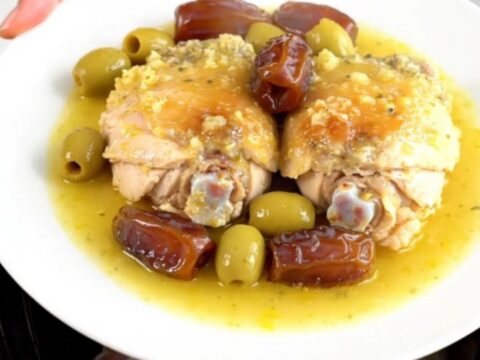 A top-down view of six raw chicken thighs arranged in a black slow cooker insert on a white speckled quartz surface.