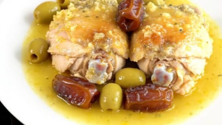 A top-down view of six raw chicken thighs arranged in a black slow cooker insert on a white speckled quartz surface.