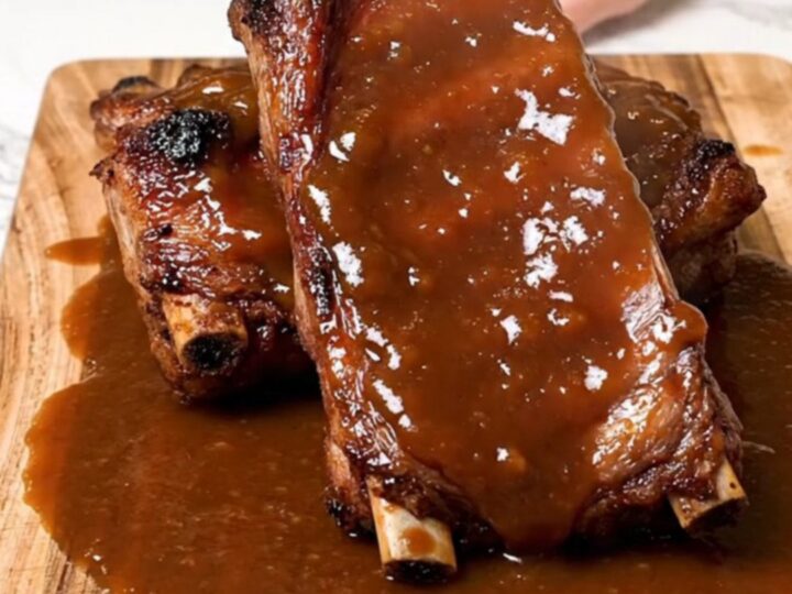 A serving of tender, glazed BBQ spareribs served on a rustic wooden board with a thick, glossy sauce.