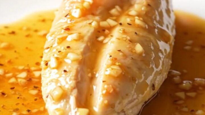 A close-up shot of cooked chicken breasts in a dark slow cooker, coated in a thick, amber honey garlic sauce.