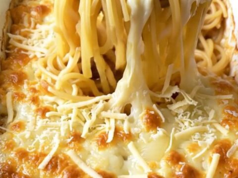 A top-down view of a cheesy French onion spaghetti bake in a white ceramic dish, featuring golden melted Swiss cheese.