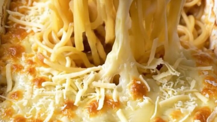 A top-down view of a cheesy French onion spaghetti bake in a white ceramic dish, featuring golden melted Swiss cheese.