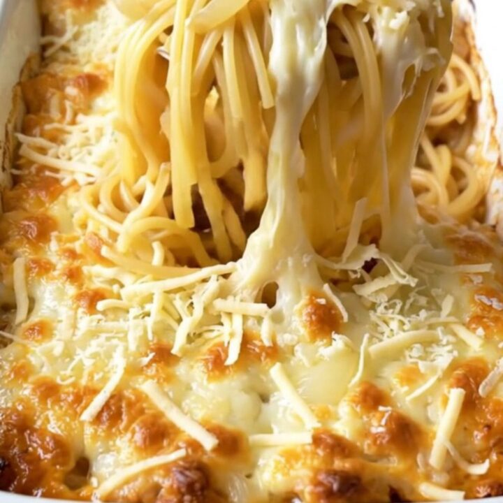 A top-down view of a cheesy French onion spaghetti bake in a white ceramic dish, featuring golden melted Swiss cheese.