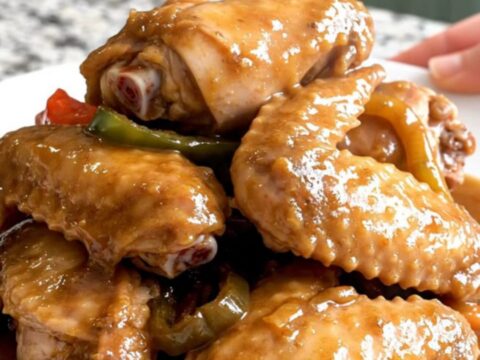 Close-up of slow-cooked turkey wings smothered in a thick, savory brown gravy with onions and peppers.