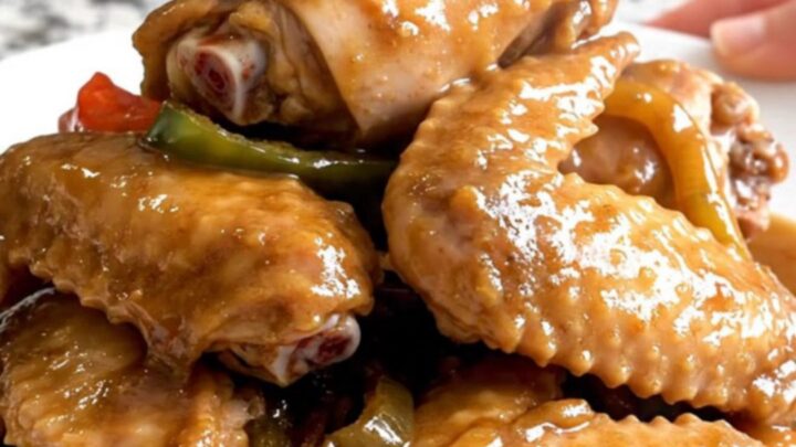 Close-up of slow-cooked turkey wings smothered in a thick, savory brown gravy with onions and peppers.