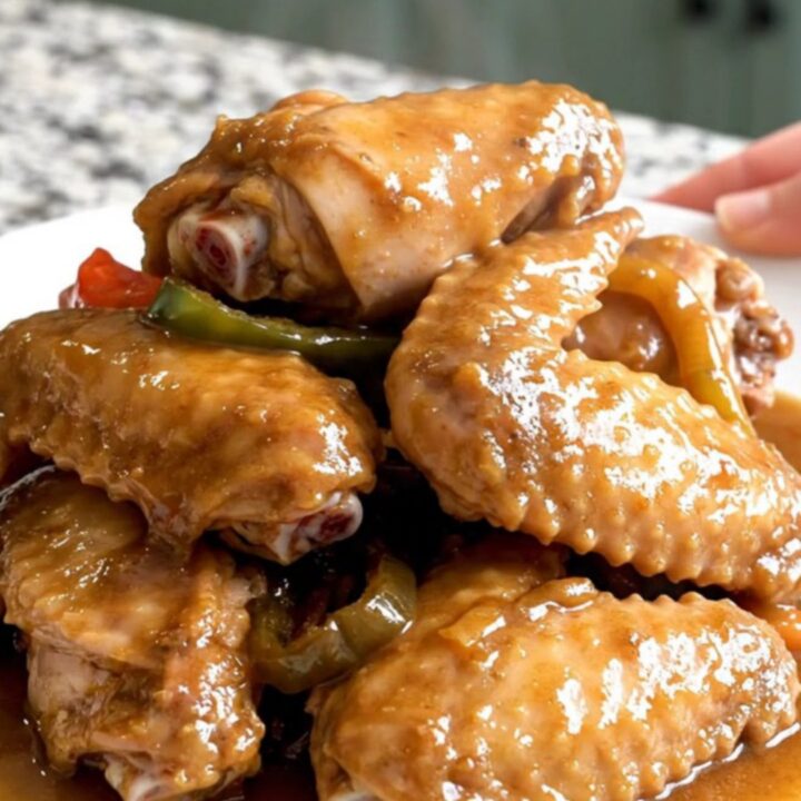 Close-up of slow-cooked turkey wings smothered in a thick, savory brown gravy with onions and peppers.