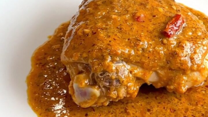 A close-up shot of creamy slow cooker chicken thighs in a black ceramic insert with a serving spoon.