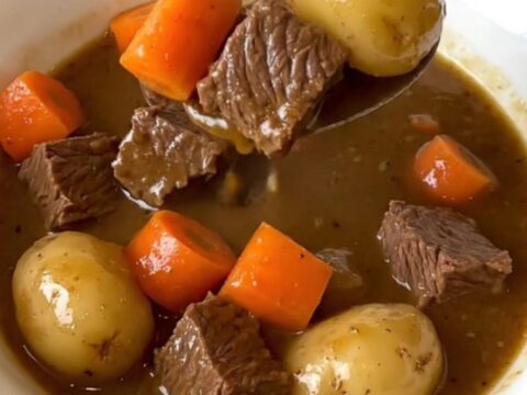 A close-up shot of a white bowl filled with tender beef chunks, potatoes, and carrots in a rich brown gravy.