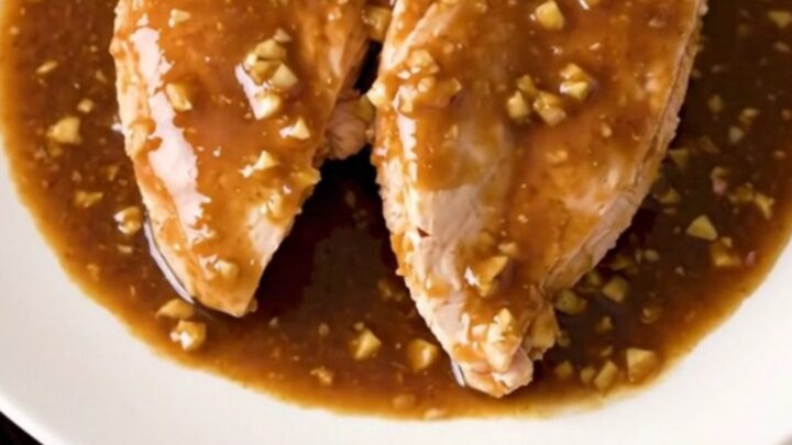 Slow cooker filled with whole chicken breasts coated in a thick, glossy brown sugar and garlic sauce.