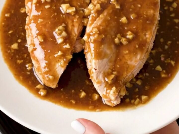 Slow cooker filled with whole chicken breasts coated in a thick, glossy brown sugar and garlic sauce.