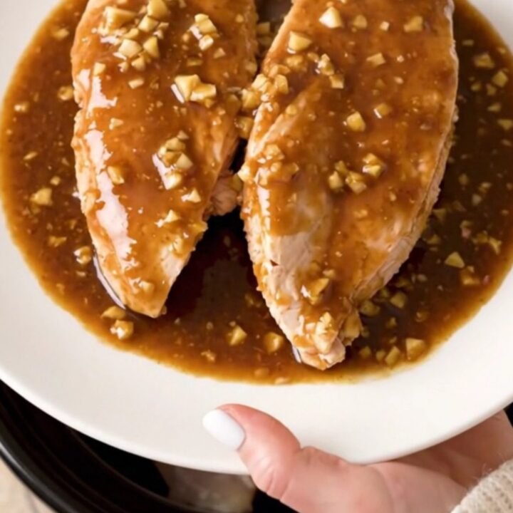 Slow cooker filled with whole chicken breasts coated in a thick, glossy brown sugar and garlic sauce.