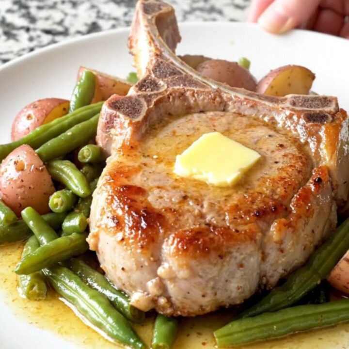A plate featuring a tender, braised bone-in pork chop with soft green beans and baby potatoes in a light butter sauce.