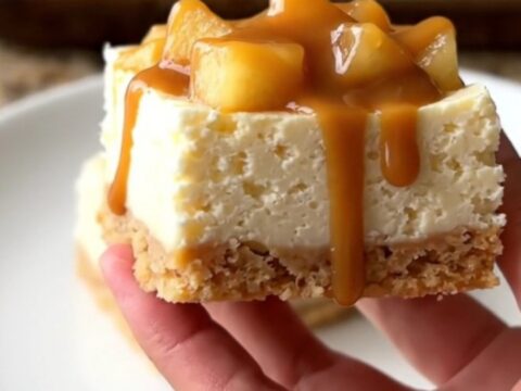 A close-up of no-bake cheesecake squares topped with apple pie filling and caramel on a baking sheet.