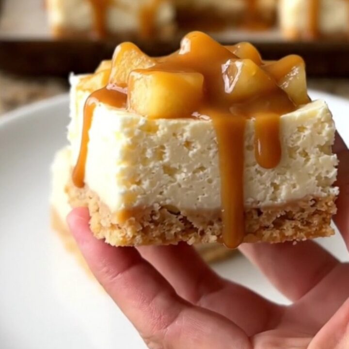 A close-up of no-bake cheesecake squares topped with apple pie filling and caramel on a baking sheet.