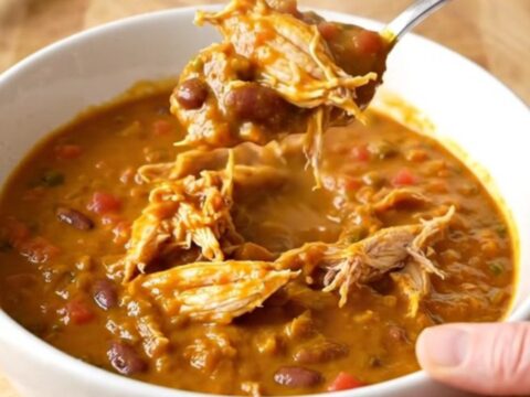 A bowl of rich, orange-red pumpkin chicken chili with shredded chicken and beans.