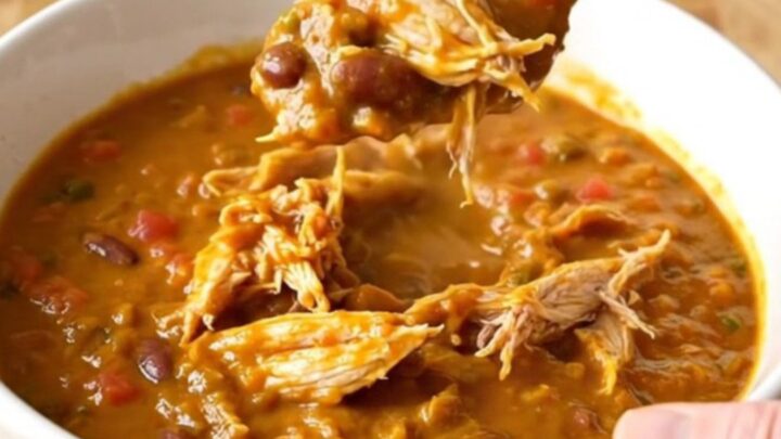 A bowl of rich, orange-red pumpkin chicken chili with shredded chicken and beans.