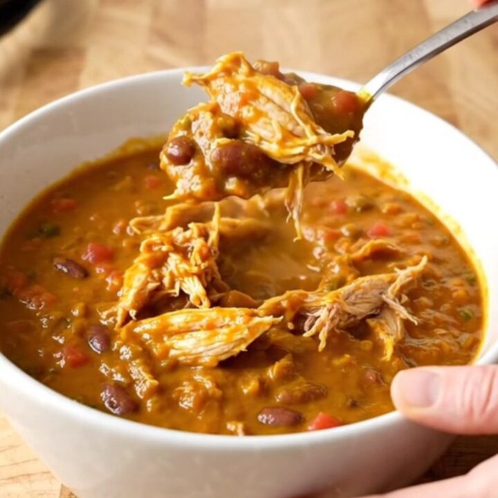 A bowl of rich, orange-red pumpkin chicken chili with shredded chicken and beans.