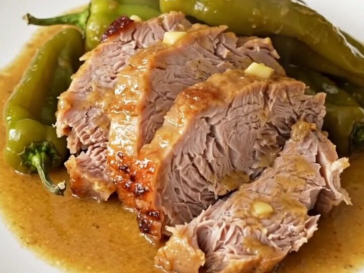 A tender, slow-cooked Mississippi pork loin served on a white plate with pepperoncini and buttery sauce.